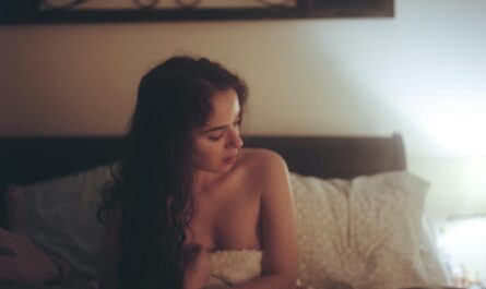 Topless Woman With White and Red Blanket on Bed With Pillows Under Brown Frame Inside White Painted Room