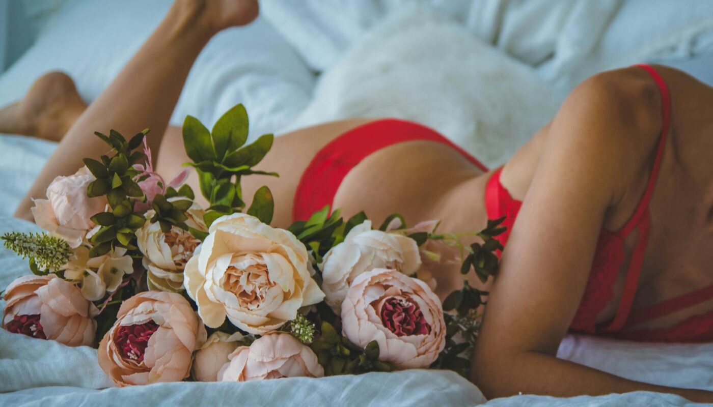 Woman in Red Two-piece Bikini Lying on Bed Beside of White and Pink Roses